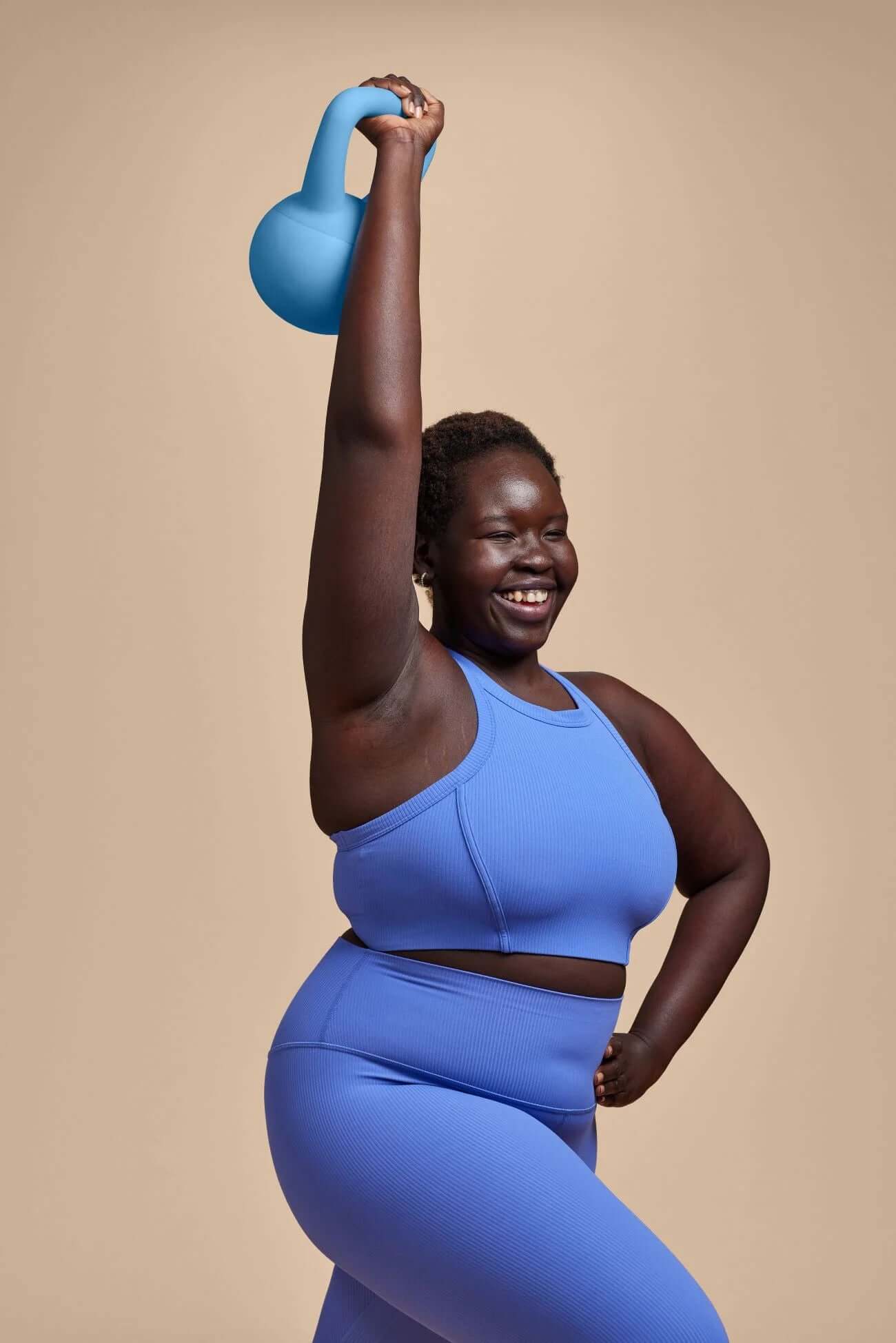 Smiling person in blue workout attire lifting a Popsugar sand-filled kettlebell for strength training.